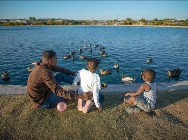 A man sits with his two kids in front of a duck pond