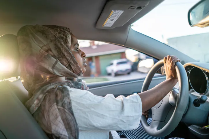 A woman drives her car (her hand is on the steering wheel)
