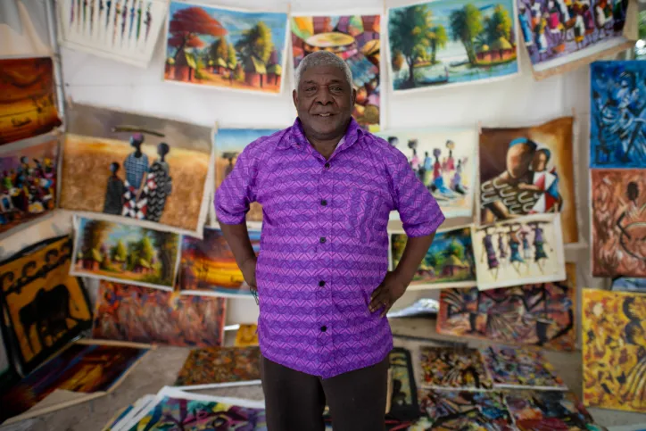 On World Refugee Day, a man stands in front of a market space made for refugee artists to showcase their paintings