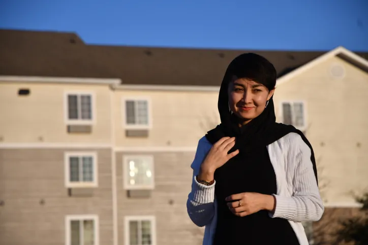 A woman stands outside her apartment building and smiles