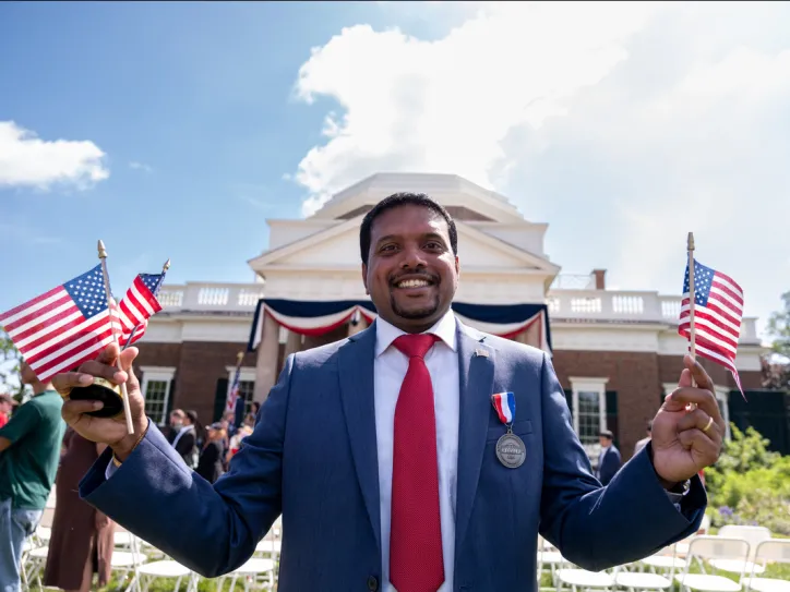 A man holds miniature American flags outside a government building and smiles