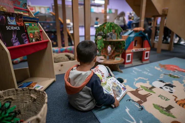A young boy (mother not pictured) reads a book in a Child Friendly Space at the IRC’s Welcome Center in Phoenix