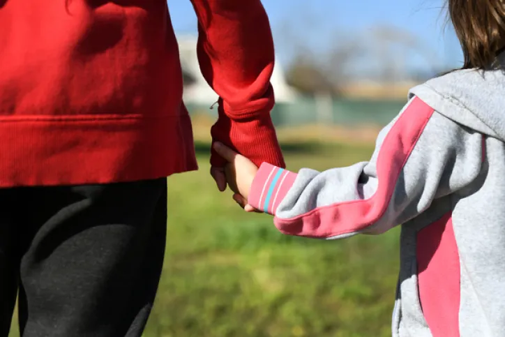 A parent and a child hold hands and stand outside