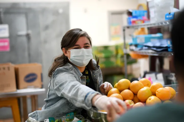 An IRC staff member wearing a face mask smiles and stands next to oranges