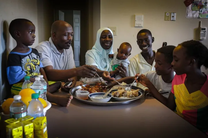 Parents and their children sit around a table in their home and share a meal together