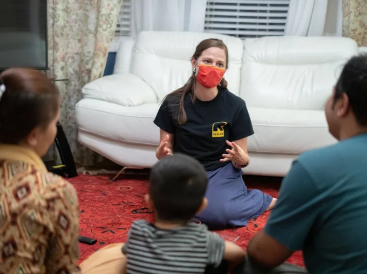 An IRC staff member sits with a resettled family in their home