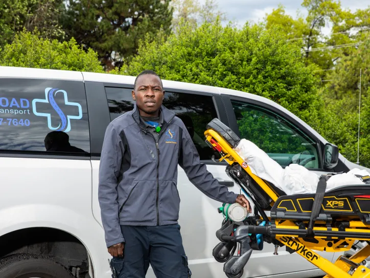A man stands next to a stretcher as part of his job as a medical transporter