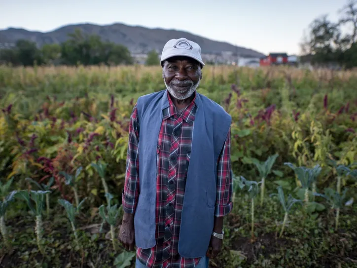 Man smiles in front of fruit and vegetable field 