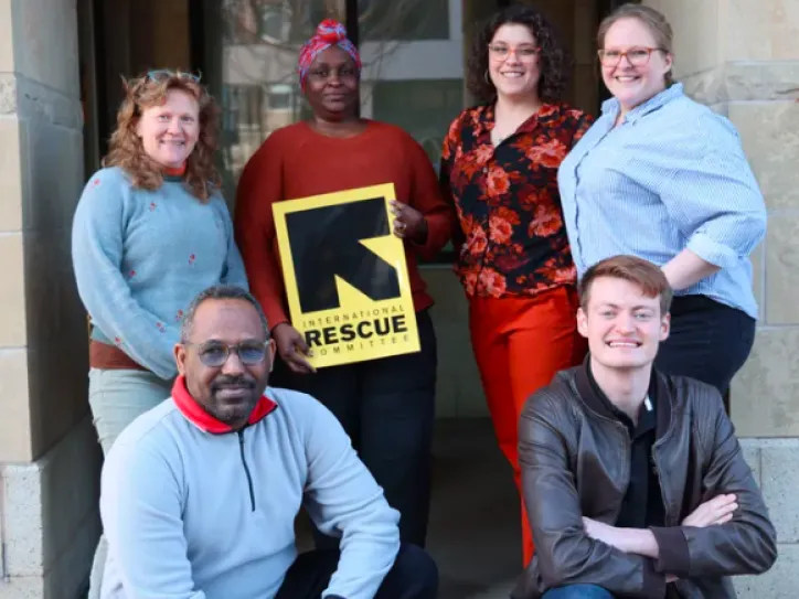 IRC in Iowa City staff members stand together for a group photo and smile; one IRC staff member holds the IRC logo