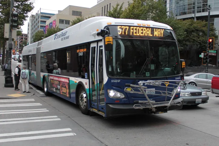 A bus drives down a Seattle street while pedestrians wait on the sidwalk