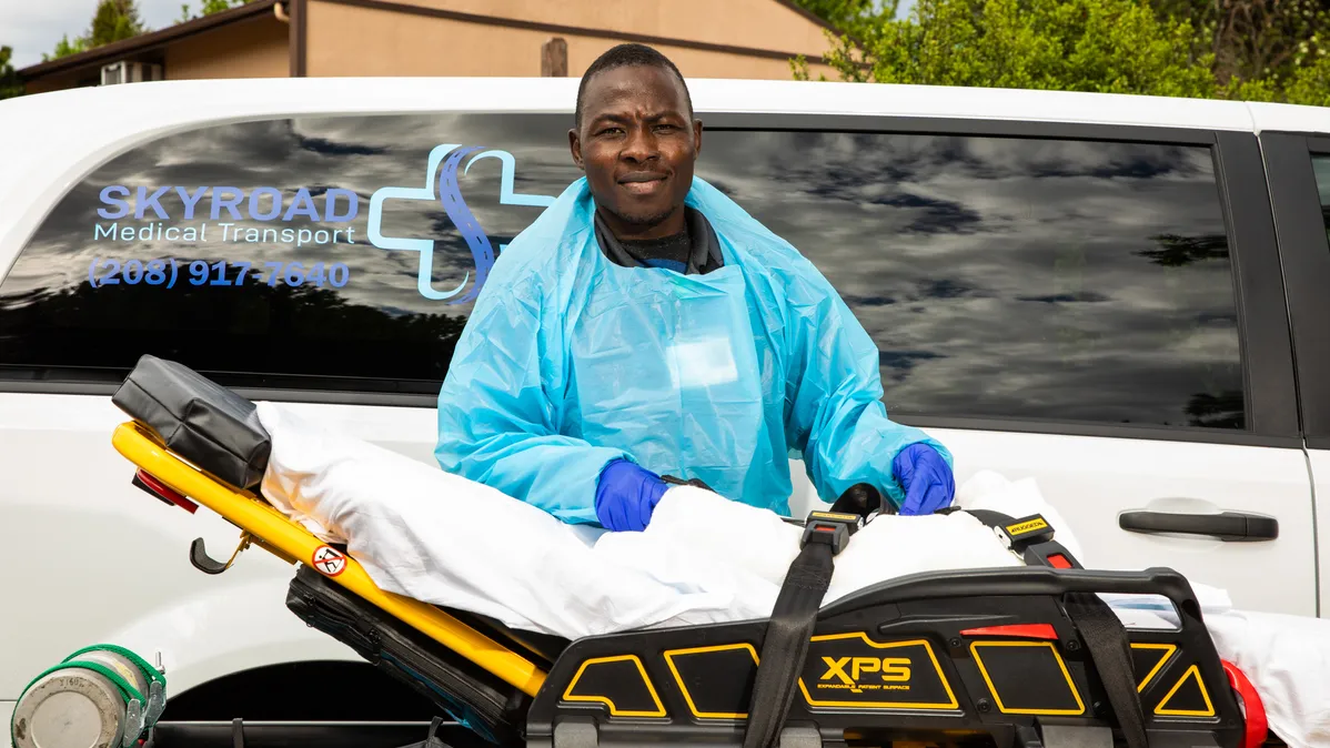 A man stands next to a stretcher as part of his job as a medical transporter