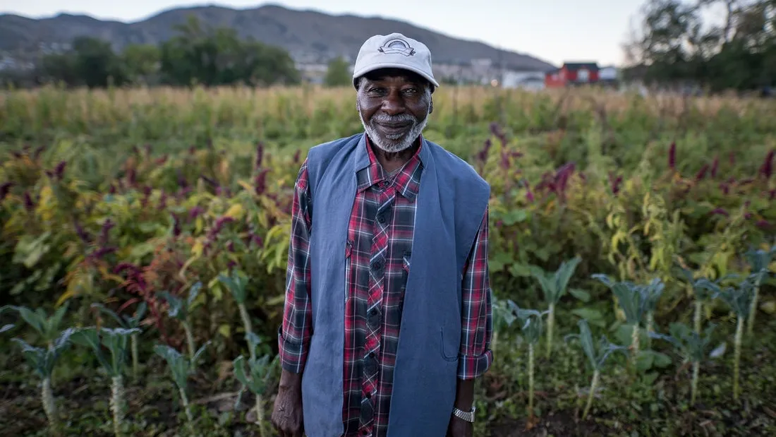Man smiles in front of fruit and vegetable field 