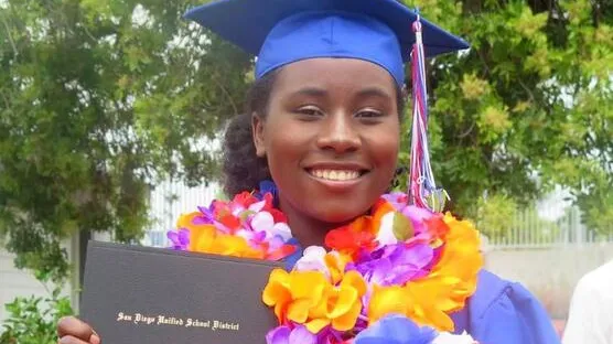 A woman holds her diploma and smiles as she graduates in her graduation gown