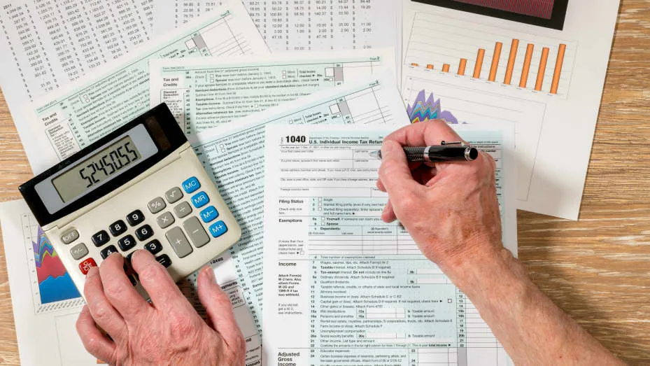 A hand writes down numbers on a tax filing page