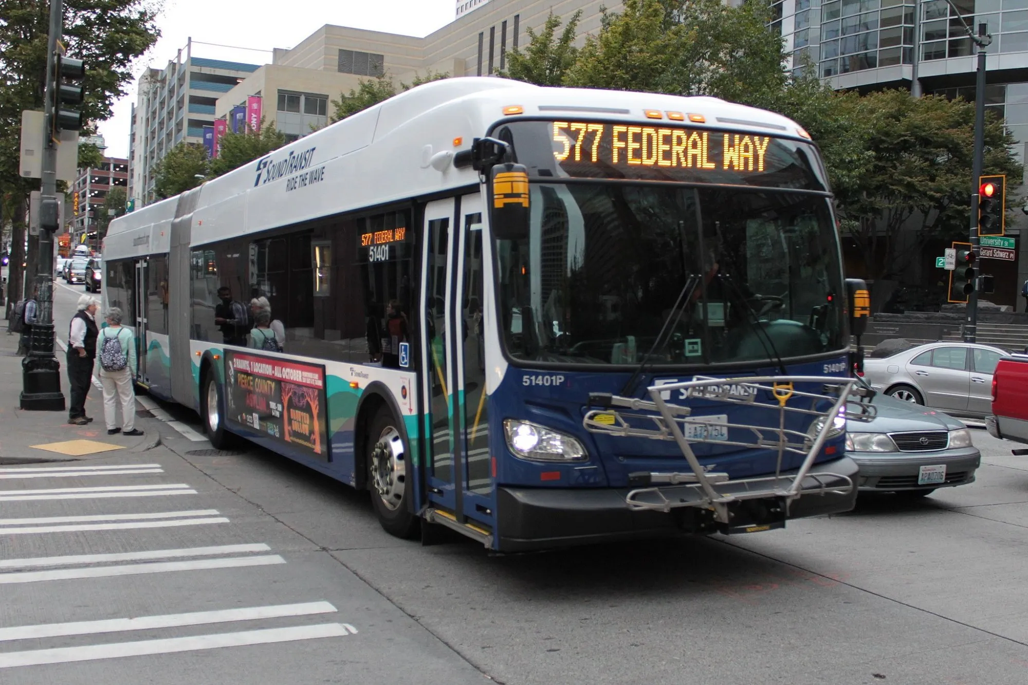 A bus drives down a Seattle street while pedestrians wait on the sidwalk